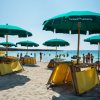 Spiaggia sabbiosa con ombrelloni verdi e sdraio gialle.