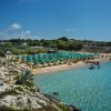 Spiaggia affollata con ombrelloni verdi, mare limpido.