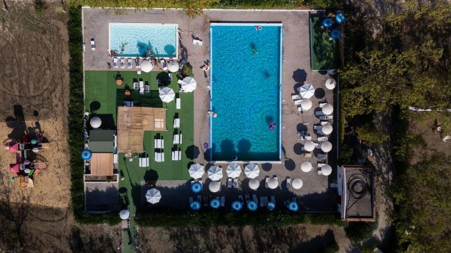 Vista aerea di due piscine con lettini e ombrelloni su un prato verde.