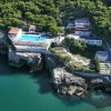 Vista aerea di un complesso con piscina su una scogliera, circondato da alberi verdi vicino al mare.