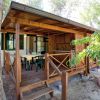 Veranda in legno con tavolo e sedie, di fronte a una casetta tra gli alberi.