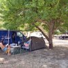 Persona seduta sotto un albero accanto a una tenda da campeggio e un furgone blu.