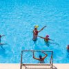 Persone giocano a pallanuoto in piscina con un pallone giallo.