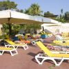 Lettini gialli sotto grandi ombrelloni bordo piscina, con persone che prendono il sole.