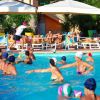 Persone che giocano in piscina sotto ombrelloni bianchi.