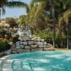 Piscina con gradini e mura di pietra, circondata da palme e vegetazione lussureggiante.