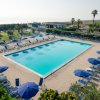 Piscina all'aperto con lettini e ombrelloni blu intorno, vista sul mare in lontananza.