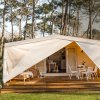 Tenda glamping con portico in legno, sedie e tavolo, immersa in un bosco.