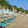 Spiaggia sabbiosa con lettini e ombrelloni a righe.