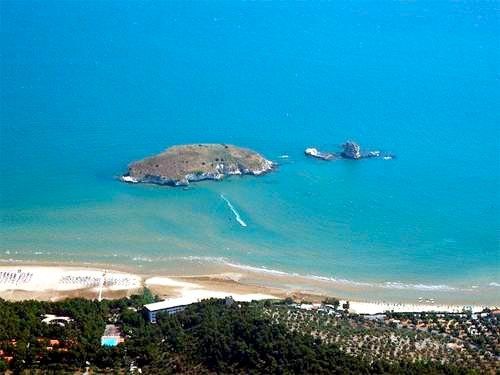 Spiaggia sabbiosa con isole in lontananza e mare blu.